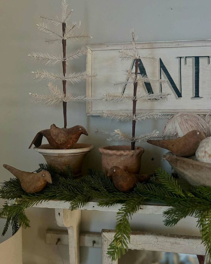 Handmade Christmas decorations with rustic birds, mini trees in pots, and greenery on a shelf.