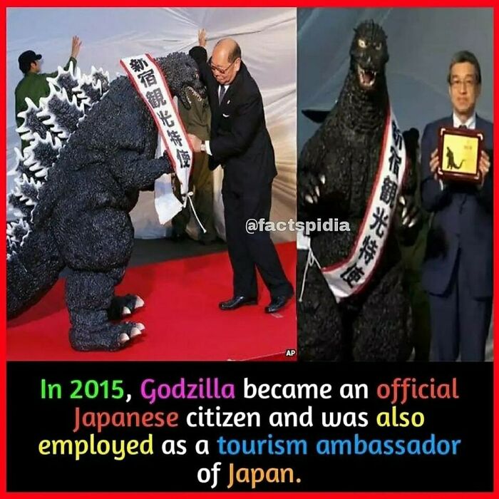 Godzilla, in costume with sash, being named a tourism ambassador of Japan in a formal setting.