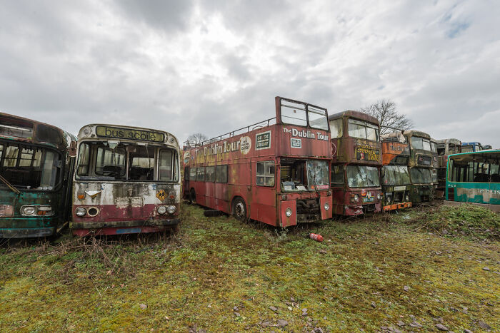 Abandoned Irish ghost buses in a graveyard, including a Dublin tour bus, set under a cloudy sky.