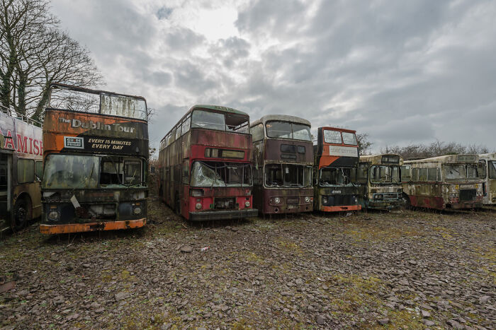 Abandoned Irish ghost buses in a graveyard under a cloudy sky.