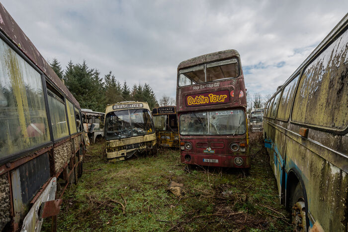 Abandoned Irish ghost buses, including a Dublin Tour bus, in a rural graveyard.