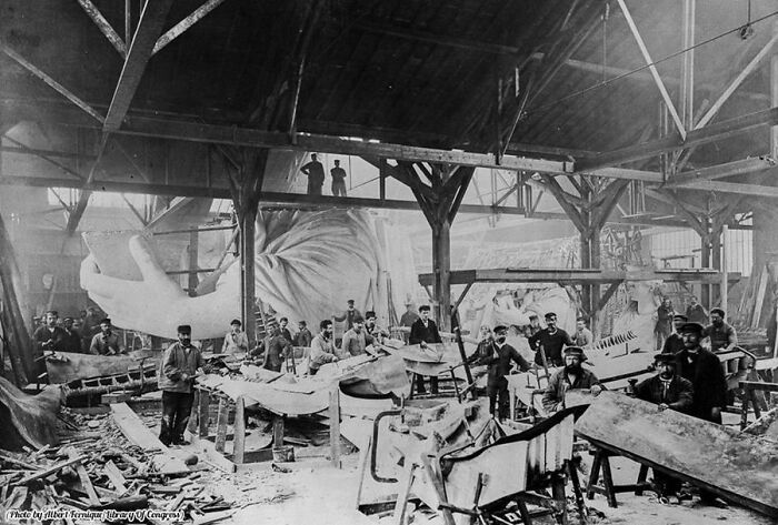 Workers assembling the Statue of Liberty in a large workshop, showcasing fascinating historical pics in black and white.