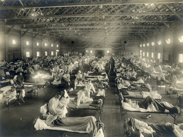 Crowded flu pandemic hospital ward showing historical impact with rows of patients and staff attending to them.