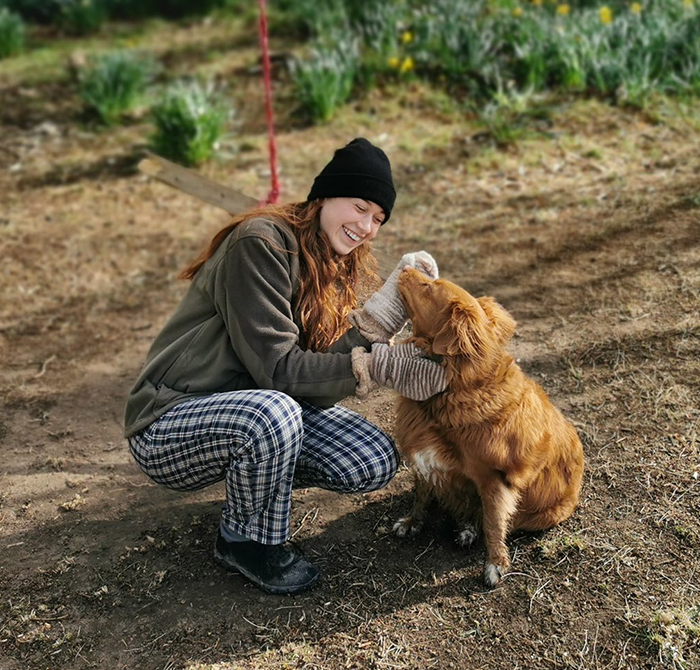 Dr. Ally Louks in a beanie plays with a dog outdoors.
