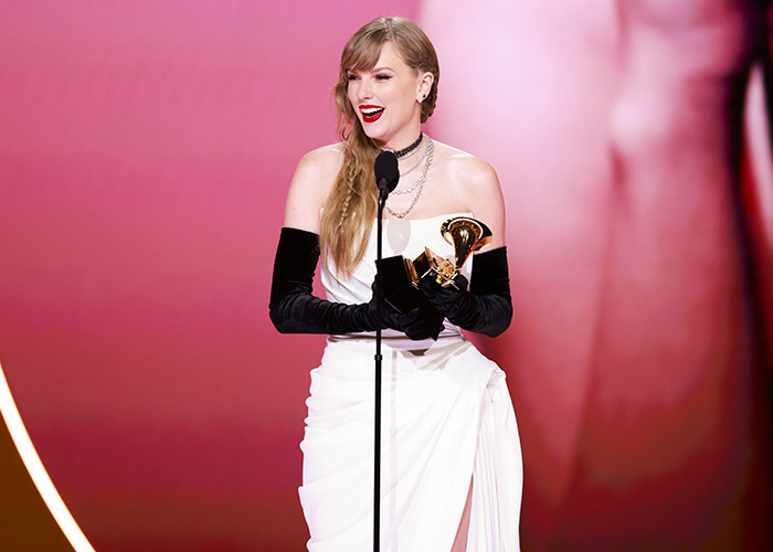 Taylor Swift in a white dress holding an award on stage.