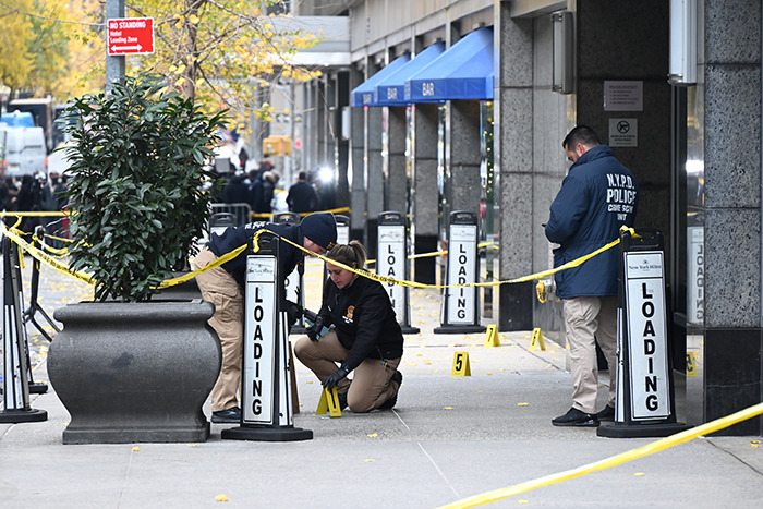 Police investigating crime scene outside a building; yellow tape and evidence markers visible, related to UnitedHealthcare CEO incident. Police investigating crime scene outside a building; yellow tape and evidence markers visible, related to UnitedHealthcare CEO incident.