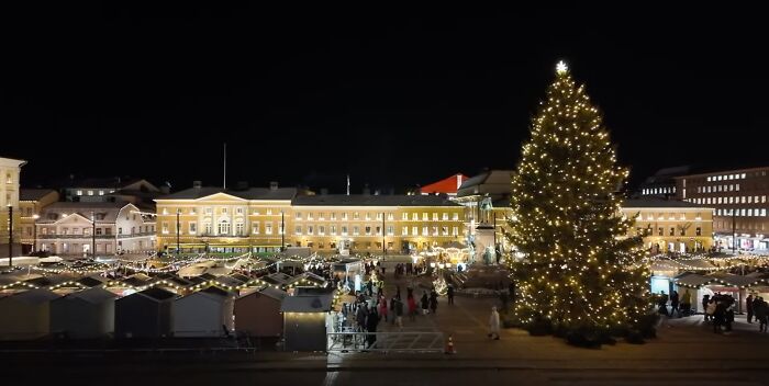 Illuminated Christmas tree in a vibrant city square at night.