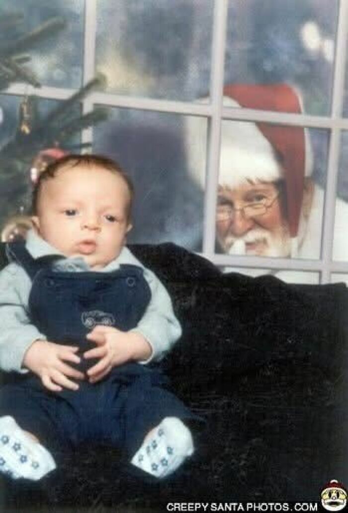 Baby sitting indoors with a creepy Santa peering through the window in the background.
