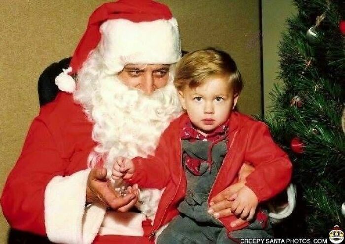 Creepy Santa holding a young child beside a Christmas tree.