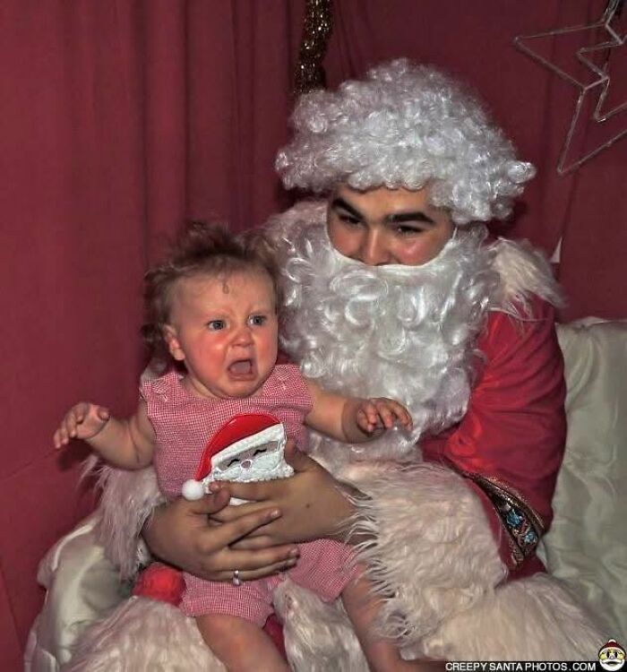 A child crying while sitting on a Creepy-Santa's lap, wearing a red outfit.
