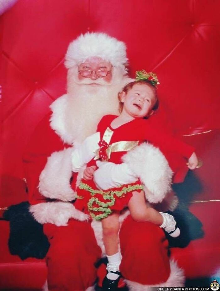 A crying child sitting on a Creepy Santa's lap, set against a red backdrop.