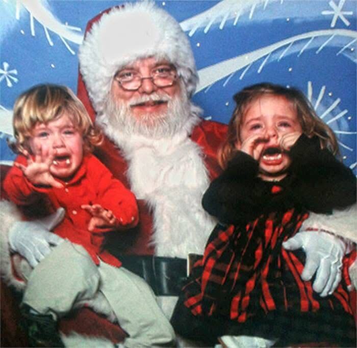 Creepy Santa posing with two crying children against a festive background.