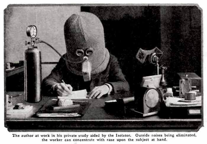 Person using strange invention called "The Isolator" helmet while writing at a desk to block out noise.