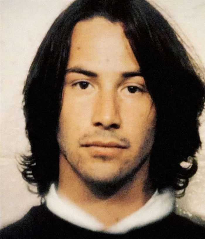 A mugshot featuring actor Keanu Reeves with long dark hair and a serious expression.
