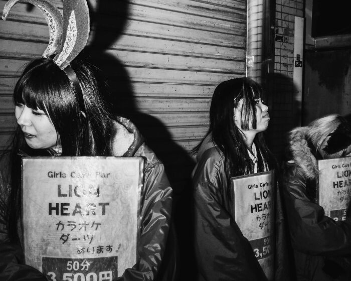 Women outside a Tokyo club in costumes, showcasing the toll of Tokyo's fast-paced life.