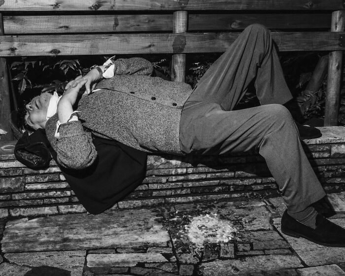 Man lying on a bench in Tokyo, reflecting the toll of a fast-paced life.