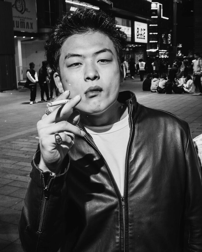 Person smoking in a busy Tokyo street at night, wearing a leather jacket.
