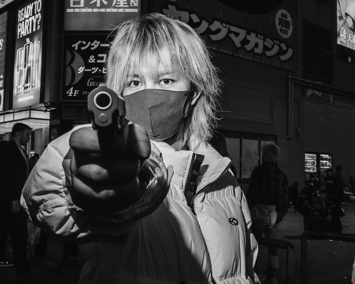 A person in Tokyo wearing a mask, holding a toy gun, highlighting the city's fast-paced life.