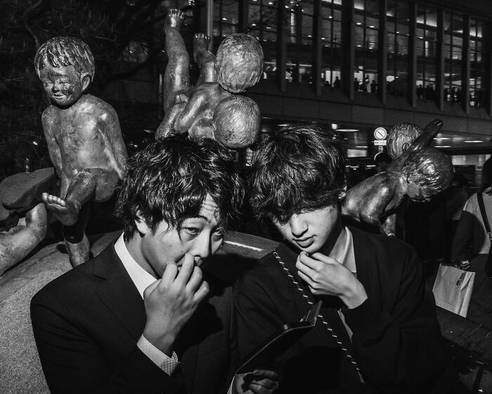 Two individuals in suits stand thoughtfully near a statue in a busy Tokyo street, capturing the city's fast-paced life.