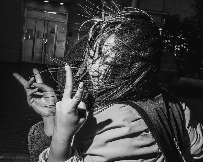 Young woman in Tokyo making peace signs, her hair blowing in the wind, capturing the city's fast-paced life.