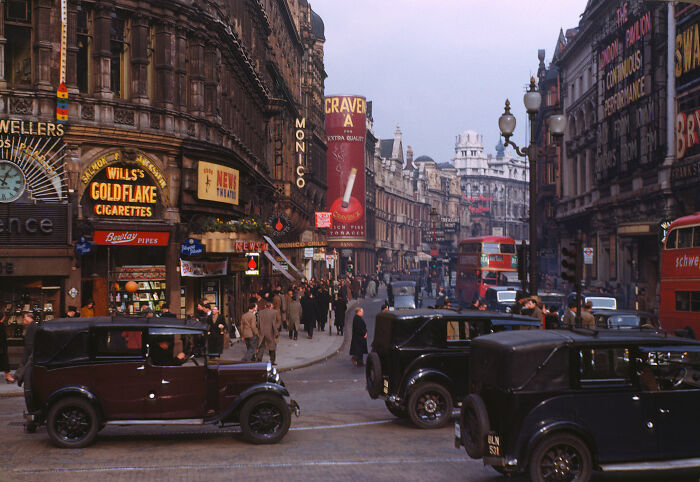Color photo of a busy 1920s city street with vintage cars, shops, and advertisements, capturing a scene from 100 years ago.