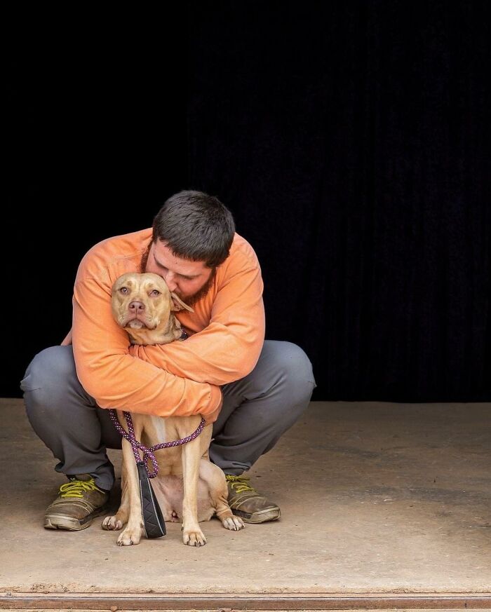 Man in an orange shirt hugging a rescued dog with a purple leash. Man in an orange shirt hugging a rescued dog with a purple leash.
