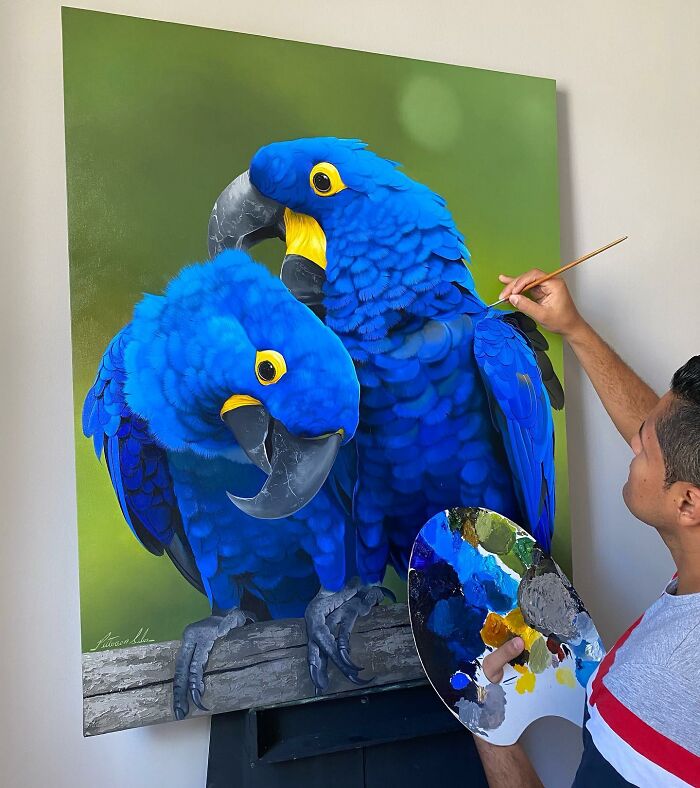 Brazilian artist painting vibrant blue parrots, showcasing fine art with feathers.