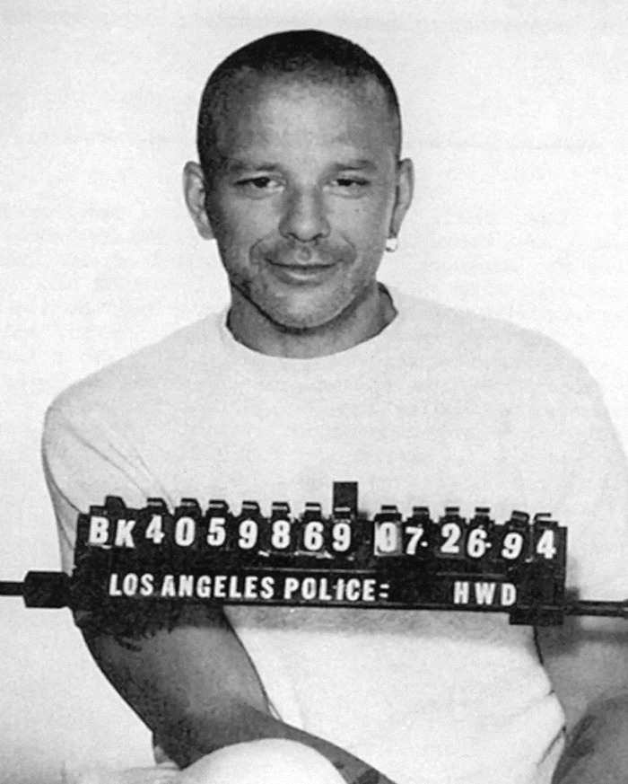 Mugshot of Mickey Rourke in a white shirt, smiling slightly, holding a Los Angeles Police sign, showcasing a viral criminal heartthrob.