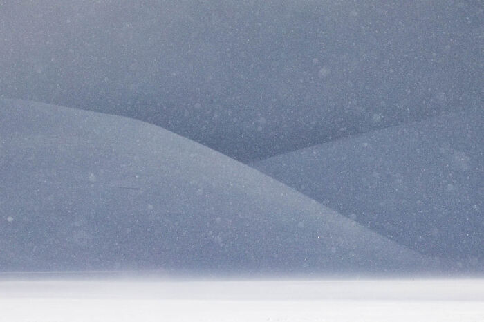 Snowy landscape showing soft hills under a gentle snowfall, capturing nature's serene beauty.