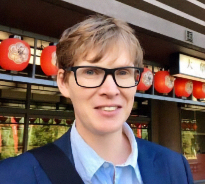 A cultural sociology expert in glasses and a blue shirt stands outside a building.