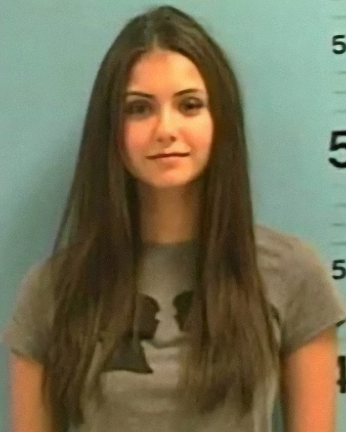 Nina Dobrev in a gray shirt against a height chart background, representing a viral mugshot of a criminal heartthrob.