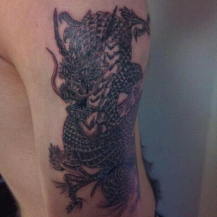 Intricate dragon tattoo on an arm with funny worst tattoo design fail.