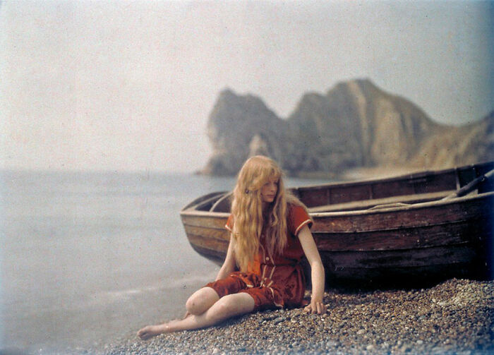 Vintage color photo of a woman sitting by a boat, showcasing life 100 years ago.