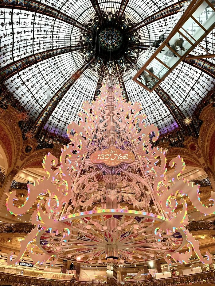 Stunning Christmas tree display in a grand city of Paris shopping center, intricate design under a glass dome ceiling.
