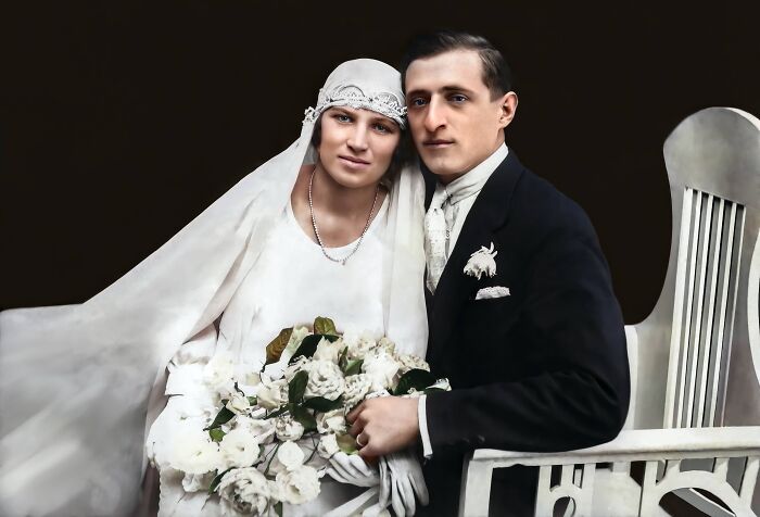 Vintage wedding photo, bride in white gown holding flowers, groom in dark suit, colorized to show how world looked 100 years ago.