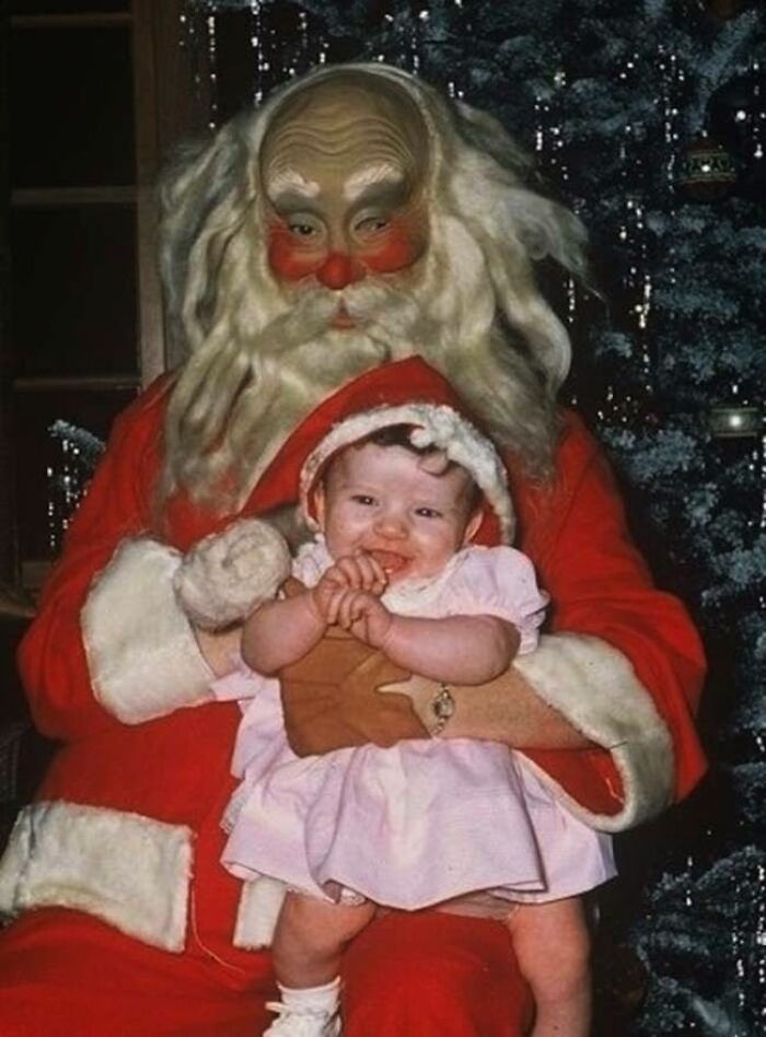Creepy-Santas: Eerie Santa with a baby in festive attire, sitting on his lap in front of a Christmas tree.