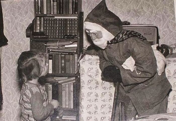 A child looking at a person in a creepy Santa costume beside a bookshelf.