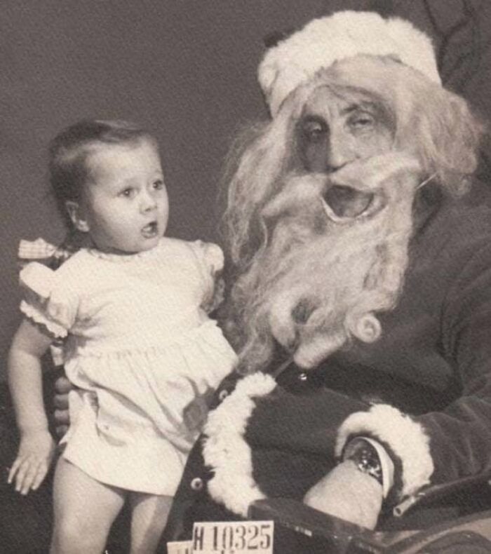 Child looking uneasy while sitting on a creepy Santa's lap in an old black-and-white photo.