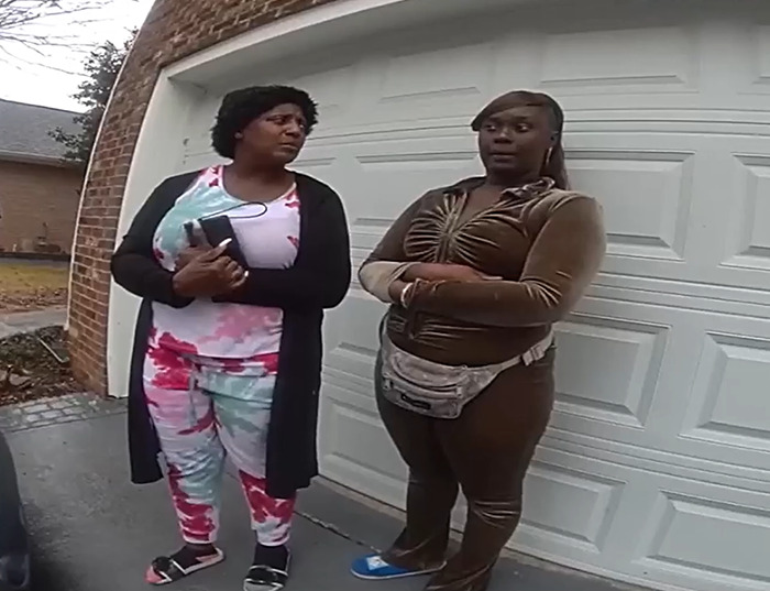 Two women standing outside a garage, discussing a home dispute involving a squatter. Two women standing outside a garage, discussing a home dispute involving a squatter.