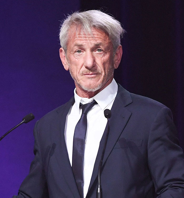 Sean Penn, dressed in a suit, speaking into a microphone at an event. Sean Penn, dressed in a suit, speaking into a microphone at an event.