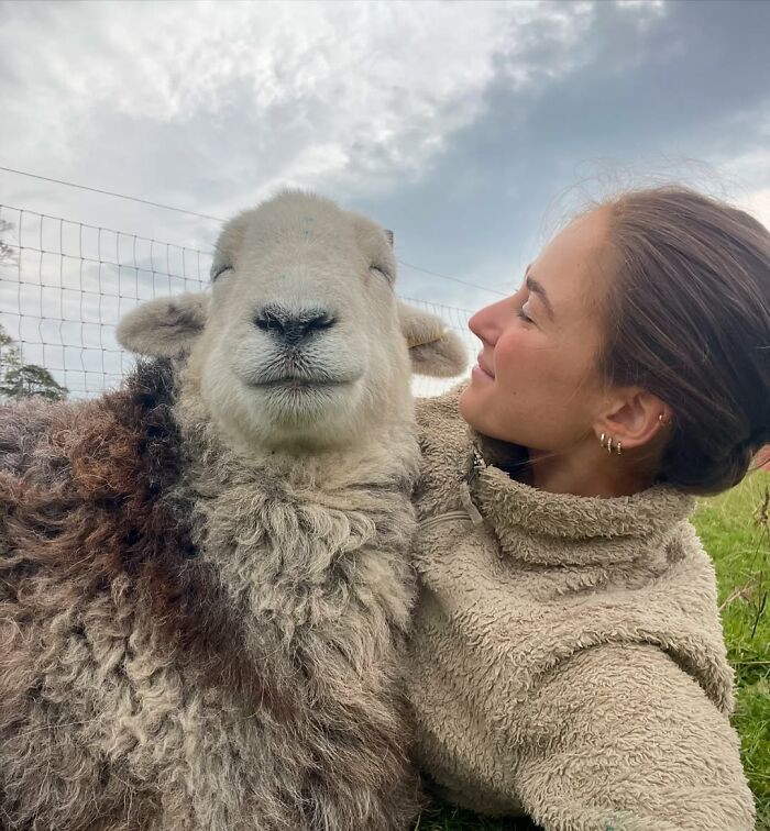 Woman smiling at a sheep in a field, showcasing a unique bond.