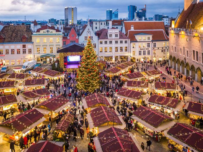 Festive Christmas tree at a bustling holiday market in a European city square, surrounded by people and lit stalls.