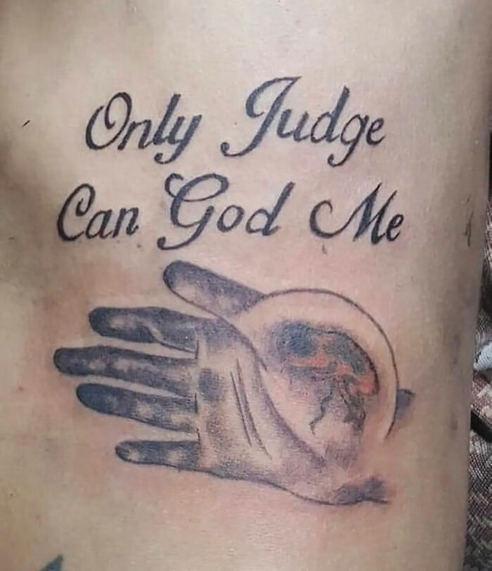 Bad tattoo with misspelled phrase "Only Judge Can God Me" and an unclear hand design on skin.