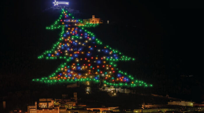 Christmas tree lights illuminate a hillside above a city at night in Italy.