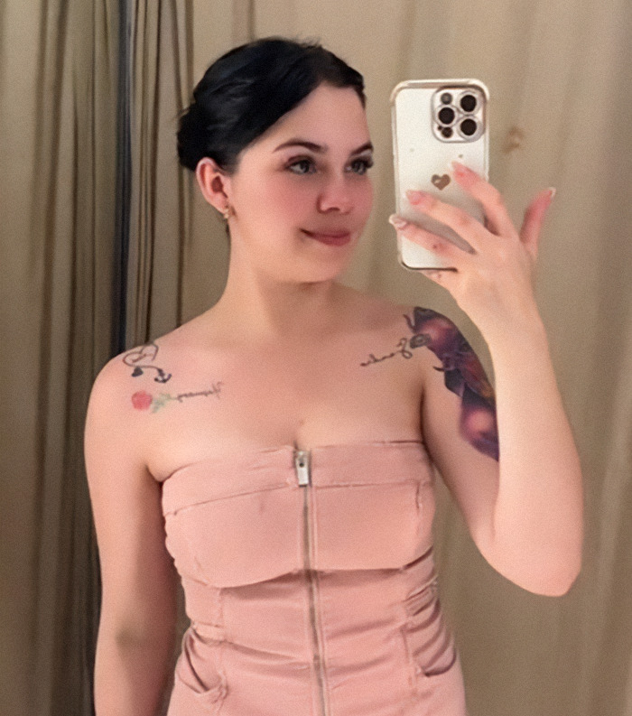 Nebrazkha in pink dress takes a mirror selfie, tattoos visible on shoulders.