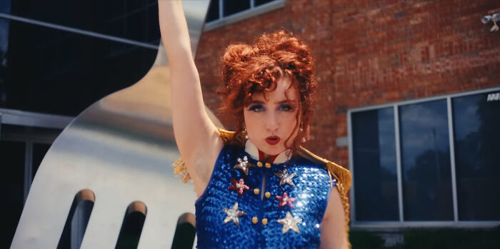 Red-haired person in a sequined blue outfit poses with raised arm, highlighting people list trends.