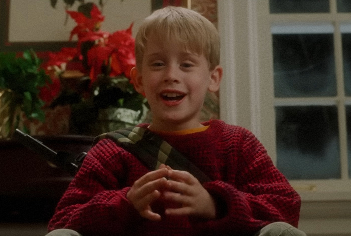 Kevin McCallister in a red sweater smiling inside a large, festive home, linked to theories about affording a huge mansion.
