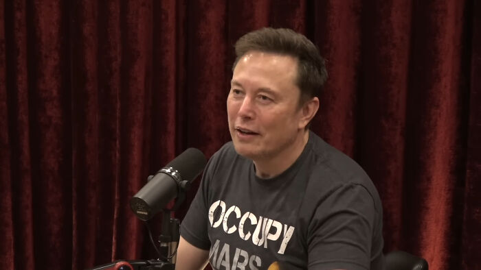 Man in "Occupy Mars" shirt speaking into a microphone, discussing trends.