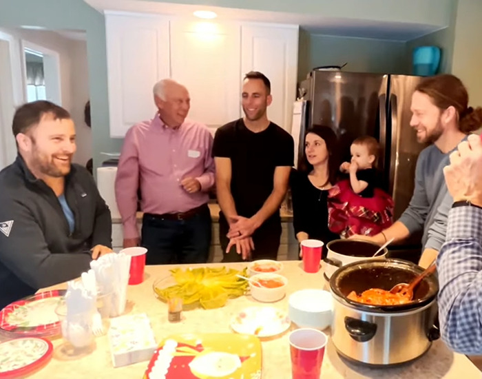 Reunion after 75 years: a man joyfully reunites with family around a kitchen table, sharing a meal and laughter.
