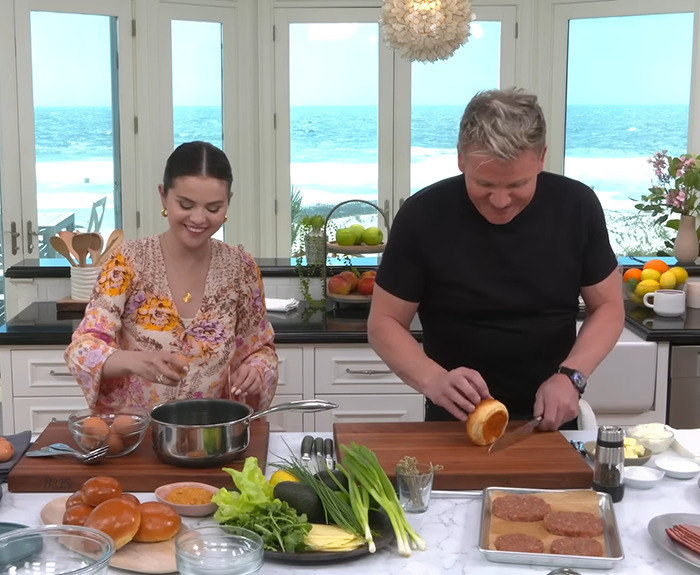 Gordon Ramsay and Selena Gomez cooking together in a bright kitchen with ocean view.